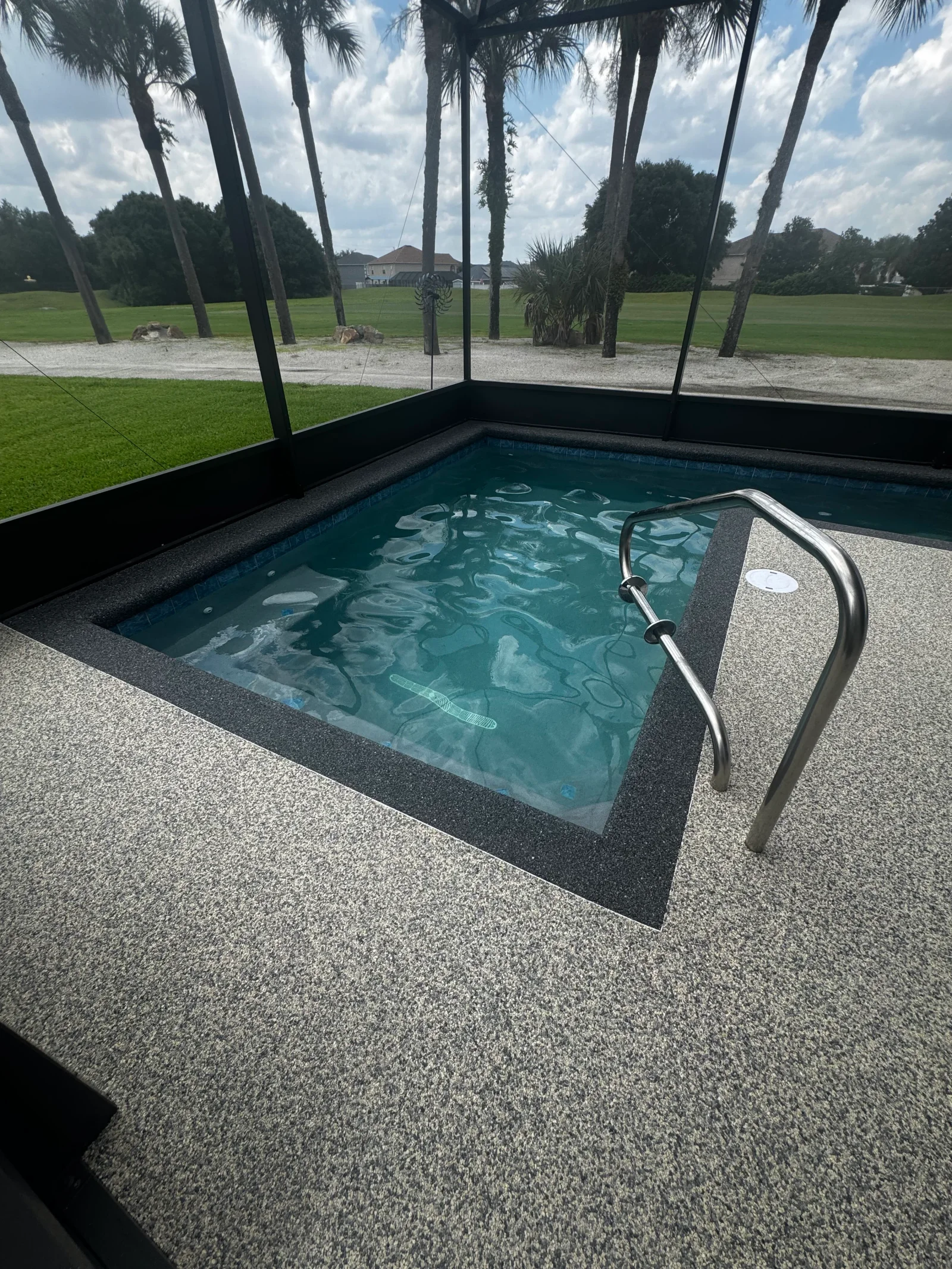 Speckled gray concrete pool deck with black border trim and stainless steel handrail