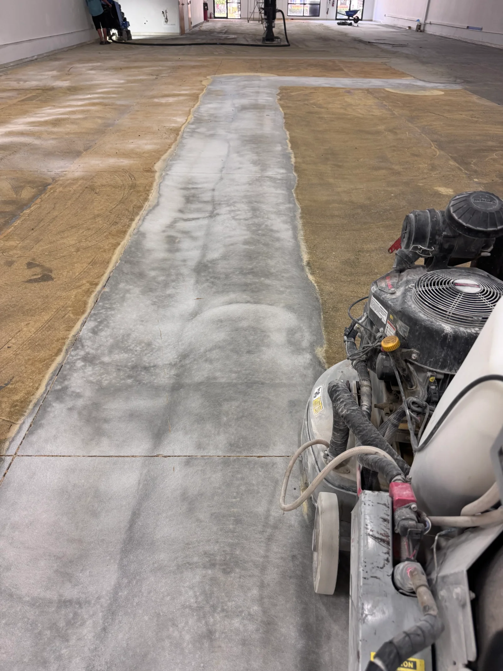 Concrete floor grinding in progress with central pathway stripped and ground smooth
