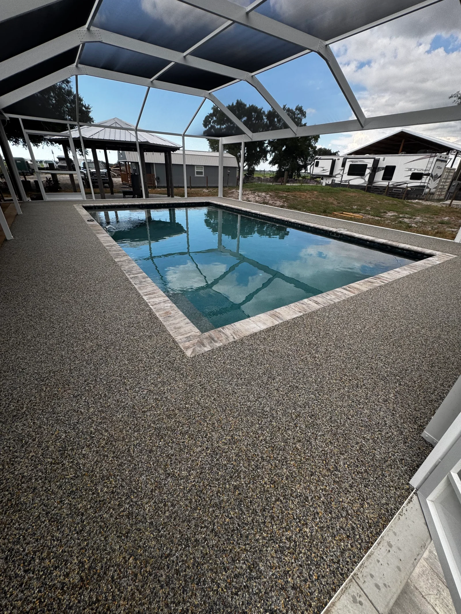 Speckled gray concrete coating on pool deck with brick border and screened enclosure